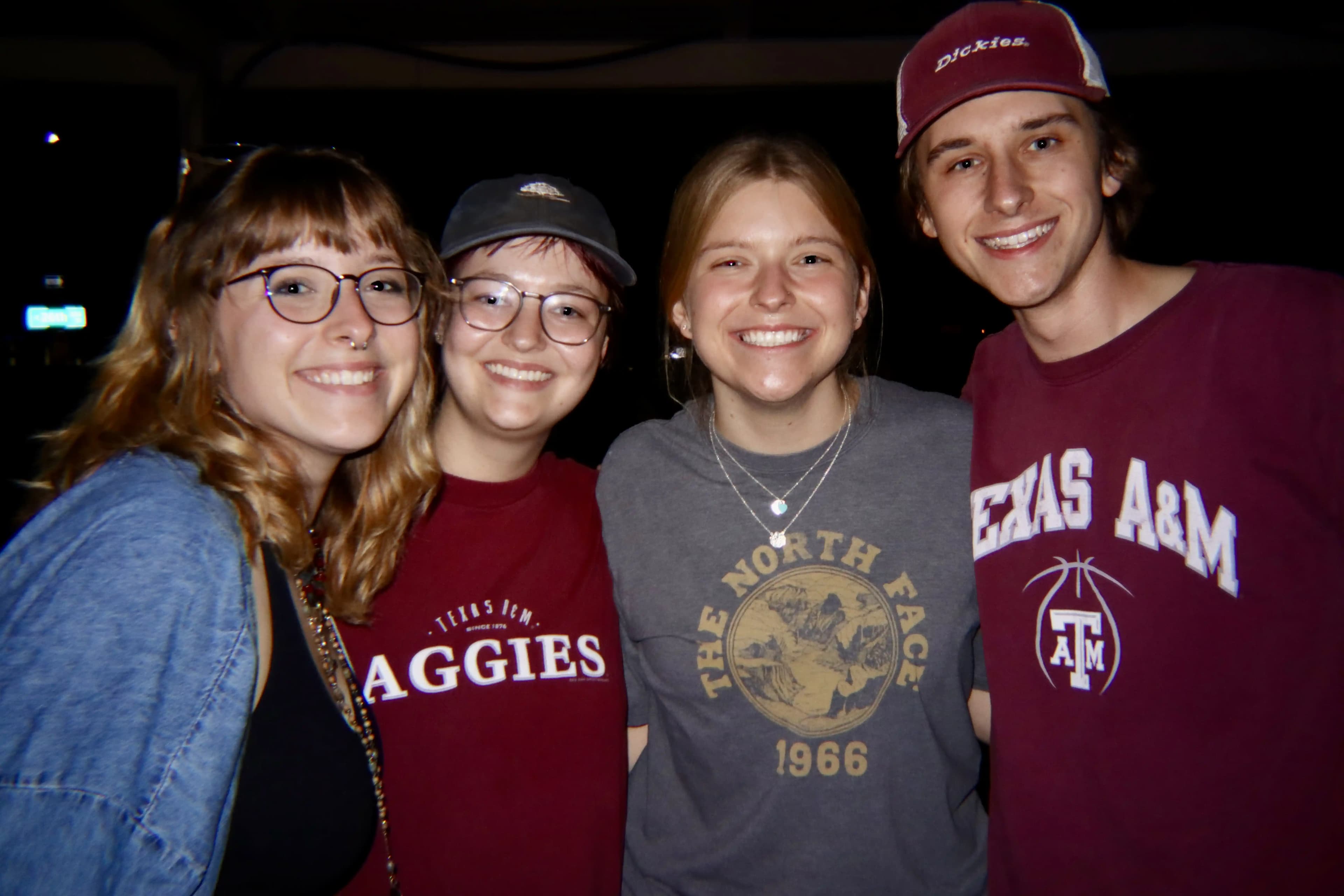 A group of four smiling students, two of them wearing Texas A&M shirts.
